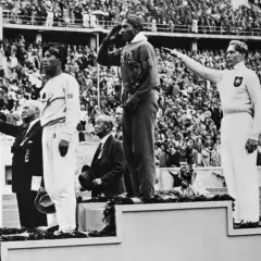 Jesse Owens hyllas på podiet vid OS i Berlin 1936. Publiken applåderar.