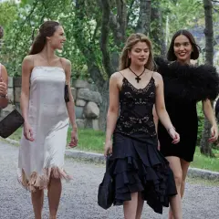Fyra unga kvinnor i eleganta klänningar, som barracuda queens, promenerar utomhus.