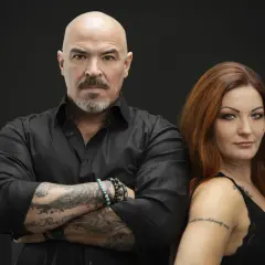 Caroline Grimwalker och en man med tatueringar och skägg står mot en svart bakgrund.