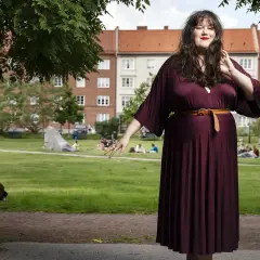 Maria Maunsbach i en vinröd klänning i en park med människor och en hund i bakgrunden.