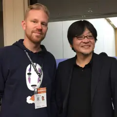 Erik Augustin Palm med en pressackreditering och en tröja med No-Face från Spirited Away, bredvid en japansk man i kostym.