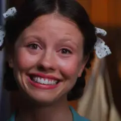 En närbild på Mia Goth som Pearl, med en bred, lite oroande leende och håret uppsatt med spets.
