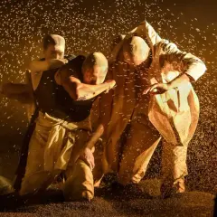 Scen från "Vredens druvor" (film). Tre personer i ljusa kläder kämpar i ett moln av damm eller korn.
