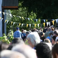 Folk samlas under flaggspel vid bokdagar i Dalsland. En man i rutig skjorta går framåt.