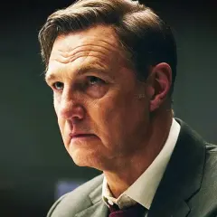 En man i kostym med rynkad panna, kanske en karaktär från nya brittiska serier.