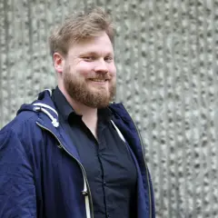 Johannes Klenell ler mot kameran, klädd i en mörkblå jacka över en svart skjorta.