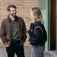 Man och kvinna pratar utanför en byggnad, kanske en scen från en svensk kin serie.