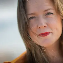 Tove Folkesson med rött läppstift och en fjäder i håret, fångad i ett mjukt ljus.