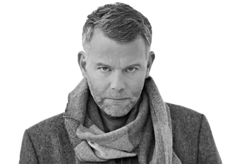 Jan Arnald, med gråmelerat hår och skägg, bär en tweedkavaj och halsduk. Kanske en scen från filmer med Jan Arnald.
