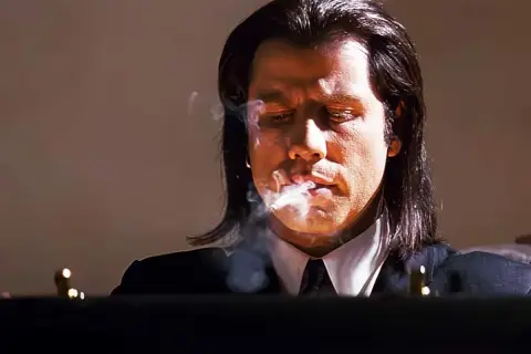 John Travolta i en ikonisk scen från filmer med John Travolta, röker och ser fundersam ut.