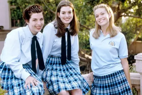 Tre glada tjejer i skoluniformer, som från en prinsessas dagbok 3. De ler mot kameran utomhus.