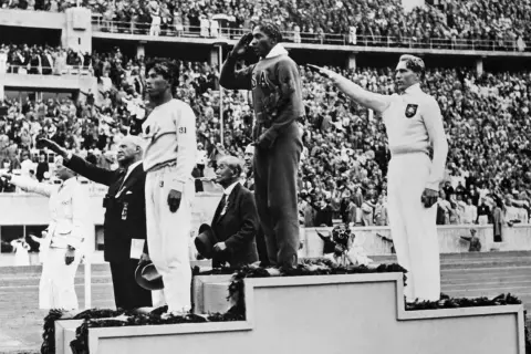 Jesse Owens hyllas på podiet vid OS i Berlin 1936. Publiken applåderar.