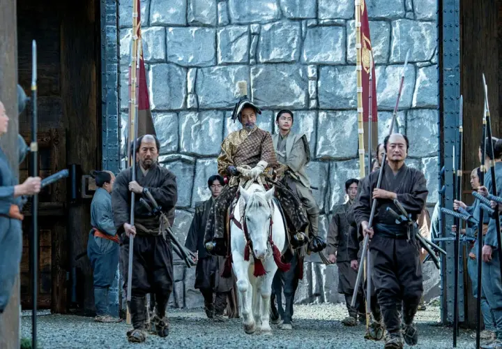 En ståtlig shogun på vit häst, omgiven av sina samurajer, anländer till en befästning. Scen från shogun serie.