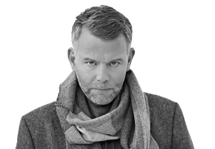 Jan Arnald, med gråmelerat hår och skägg, bär en tweedkavaj och halsduk. Kanske en scen från filmer med Jan Arnald.