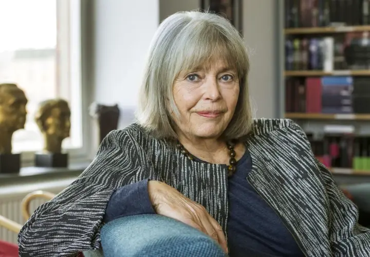 Agneta Pleijel, författare, sitter i en fåtölj med en bokhylla i bakgrunden.