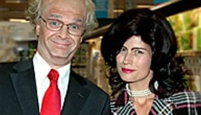 Två personer i kostym och peruk. Mannen har glasögon och röd slips, kvinnan har svart peruk och pärlhalsband. Hey baberiba!