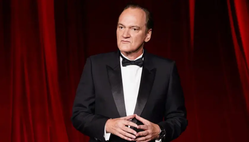 Quentin Tarantino, ikonen bakom ikoniska tarantino filmer, i en elegant smoking framför en röd ridå.