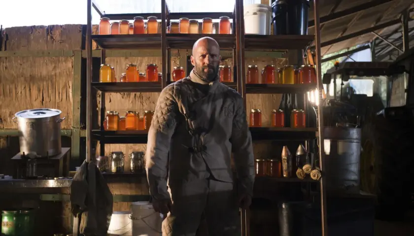 Jason Statham som rollistan i The Beekeeper, omgiven av burkar med honung och jordbruksutrustning.