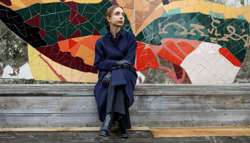 Alexandra Andersson sitter på en träbänk framför en färgglad mosaikvägg.