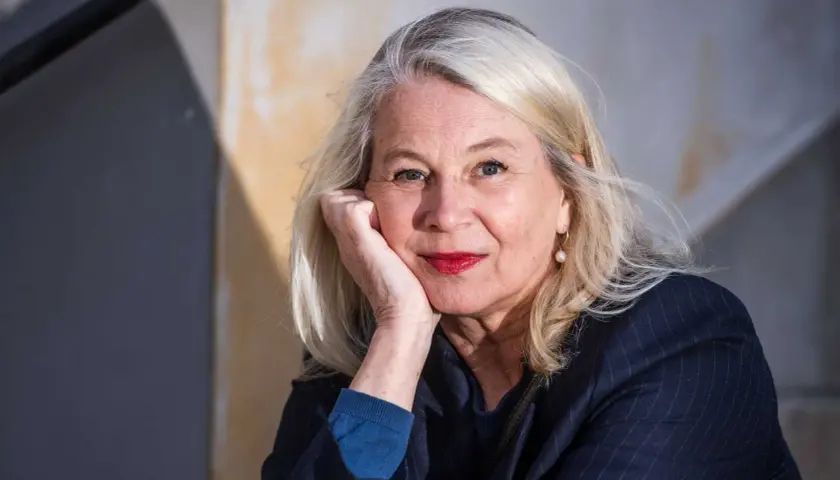 Helena von Zweigbergk, med sin partner vid sin sida, ler mot kameran. Hennes blonda hår ramar in ett ansikte med röda läppar och en pärlörhänge.