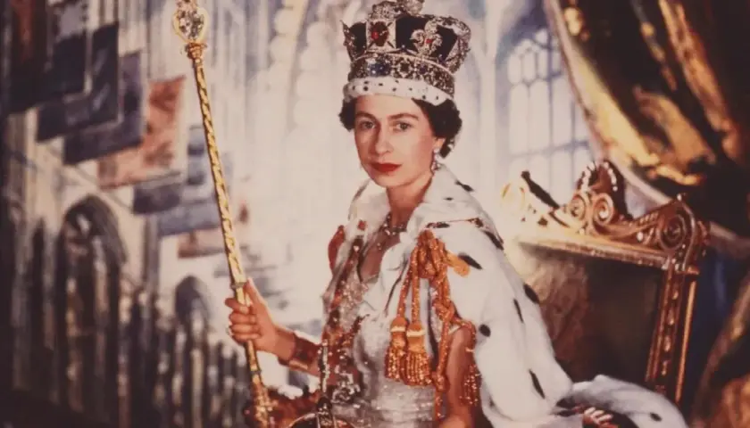Elizabeth II av Storbritannien, krönt och med spira, sitter på tronen i sin kungliga dräkt.