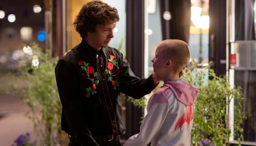 En man med blommig skjorta rör vid ett barns kind. En scen som kan ingå i svenska komedier.