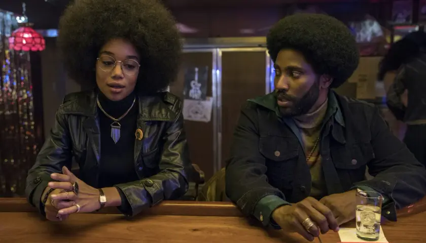 En kvinna med stor afro och en man med skägg sitter vid en bardisk. De är medlemmar i rollistan i Blackkklansman.
