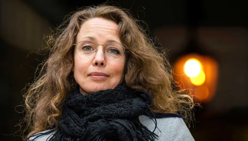 Sara Gordan dotter med sitt långa, lockiga hår och en svart halsduk. Hon bär glasögon och tittar rakt in i kameran.