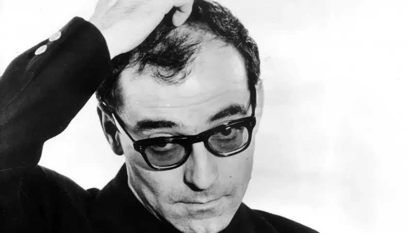 Jean-Luc Godard med handen i håret, bär glasögon och en mörk kavaj. En ikonisk bild av filmskaparen.