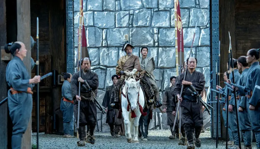 En ståtlig shogun på vit häst, omgiven av sina samurajer, anländer till en befästning. Scen från shogun serie.