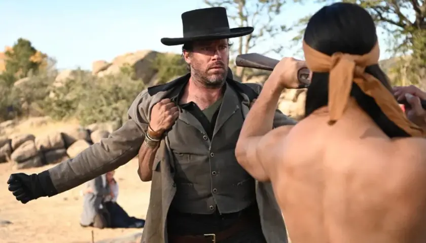 Armie Hammer i vilda västern, redo för strid. En man med bandana drar vapen.