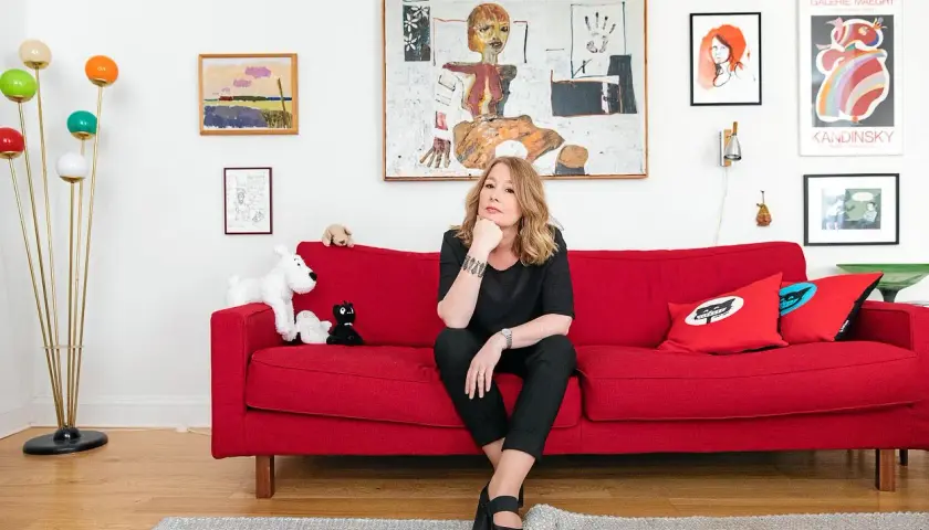 Åsa Linderborg sitter på en röd soffa, omgiven av konst och leksaker som påminner om barn.