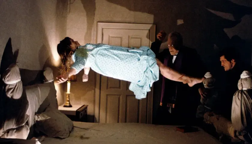 En flicka svävar i luften under en exorcism. Prästen håller hennes ben, medan en annan man ser på. En ikonisk scen från rollistan i Exorcisten.