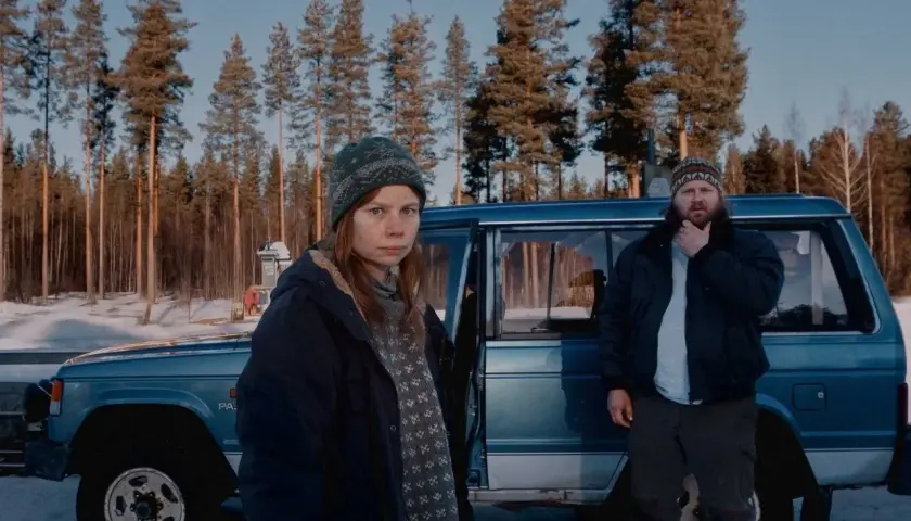 Två personer står vid en blå bil i en snöig skog. Kanske jag for ner till bror serie, och detta är en scen från den.