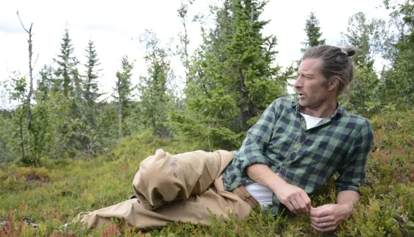 Frida Torgeby vilar i skogen, omgiven av blåbärsris och granar.