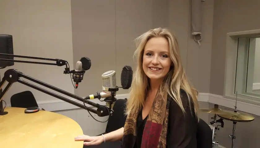 Maria Broberg ler i en radiostudio med mikrofoner och trummor i bakgrunden.