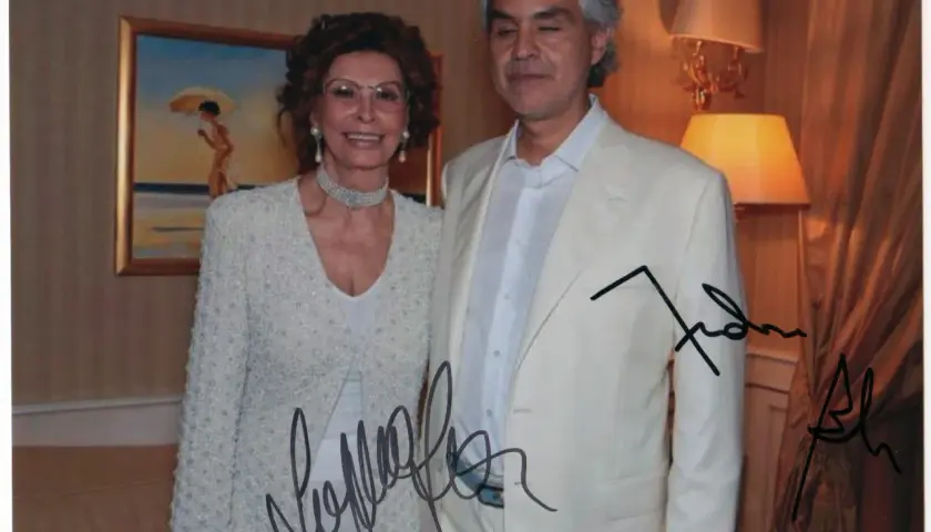 Sophia Loren and Andrea Bocelli pose for a photo, both with autographs on the image.