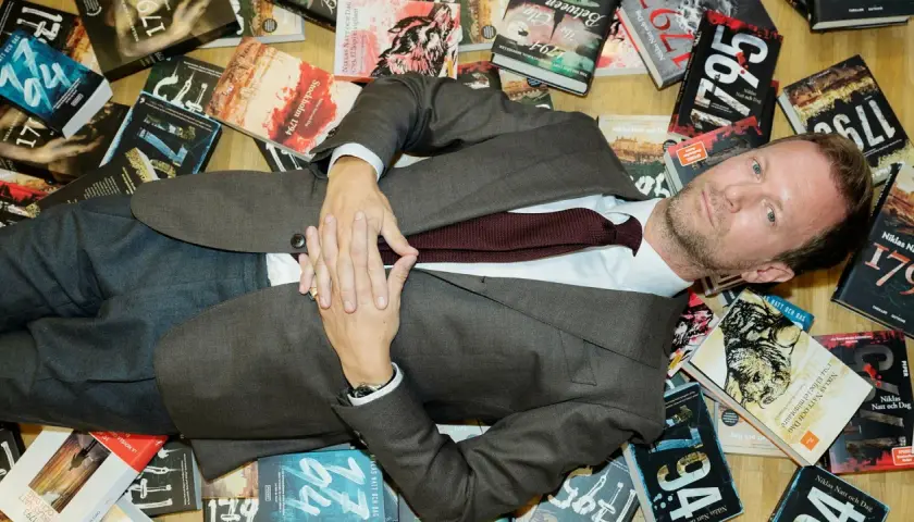 Man i kostym ligger bland böcker av Niklas Natt och Dag.