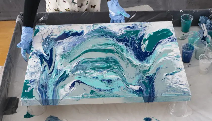 En person med blå handskar skapar en virvlande resin art-målning i blå och turkosa nyanser.