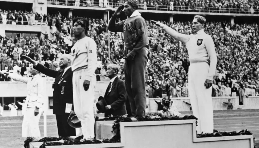 Jesse Owens hyllas på podiet vid OS i Berlin 1936. Publiken applåderar.