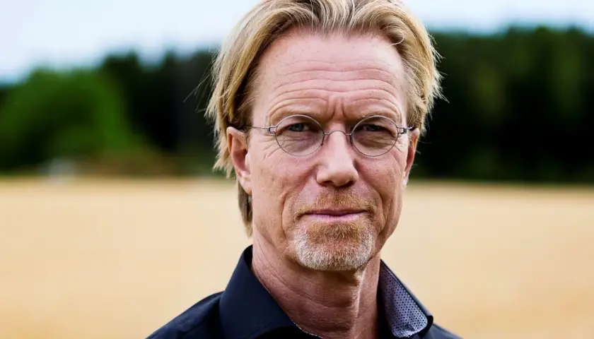 Ewert Grens, en man med blont hår och glasögon, ler mot kameran i en åker.