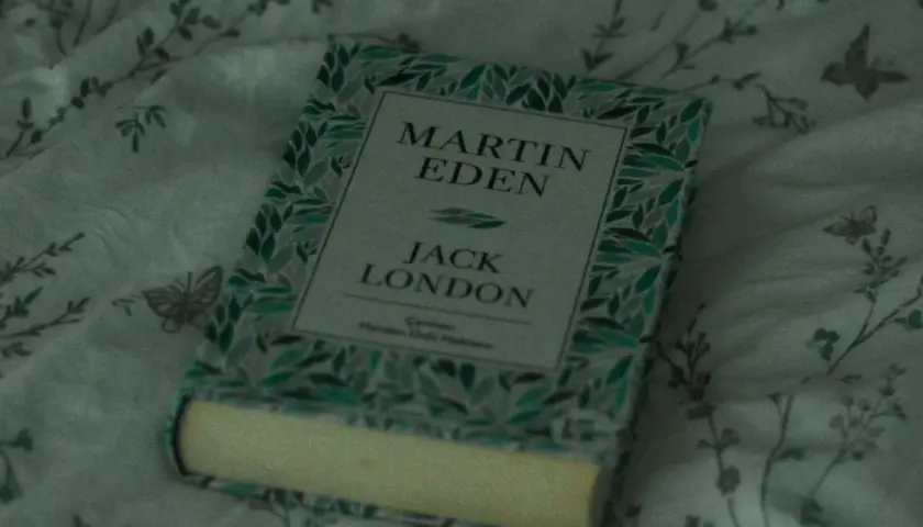 En bok med titeln "Martin Eden" av Jack London ligger på ett mönstrat tyg. Vad betyder roman? Denna bok är ett klassiskt exempel.