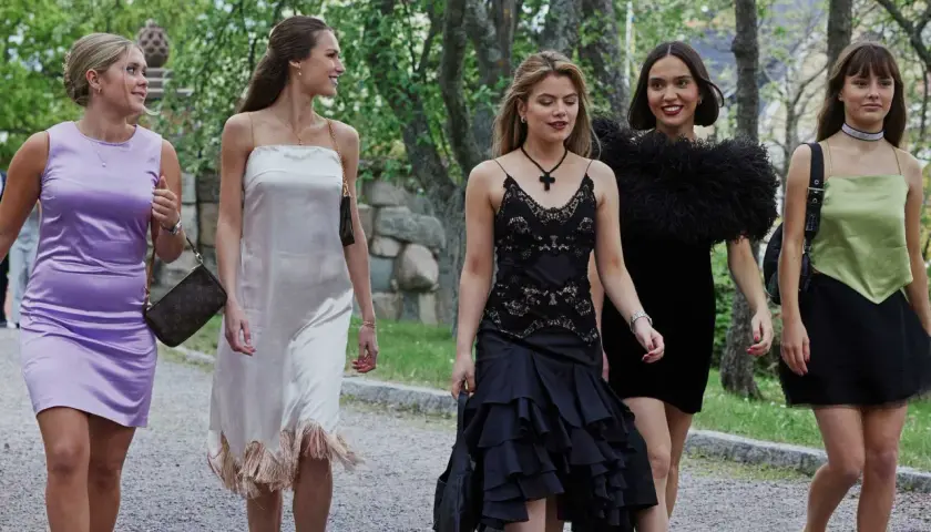 Fyra unga kvinnor i eleganta klänningar, som barracuda queens, promenerar utomhus.