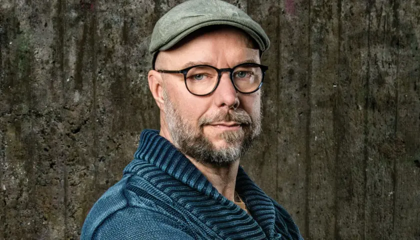 Sven Olov Karlsson, en man med glasögon och keps, blickar mot kameran. Han bär en blå stickad tröja.