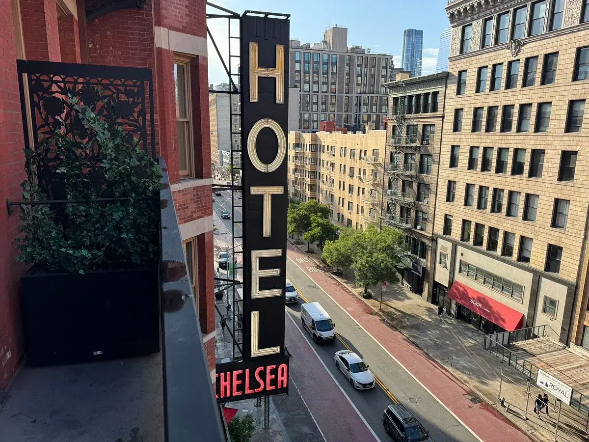 Neo-upplyst skylt för Chelsea Hotel, med en balkong med växter i förgrunden.