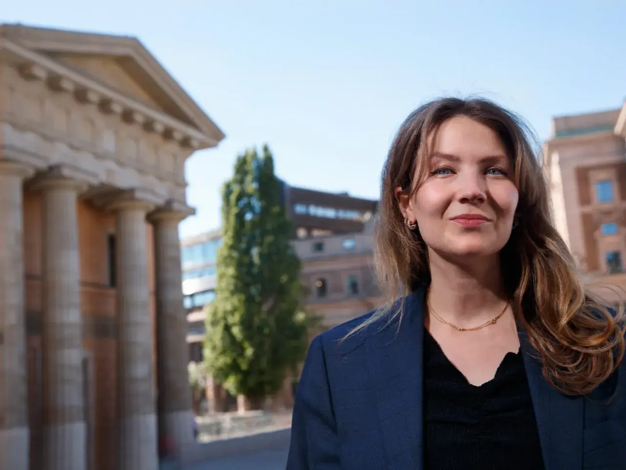 Cecilia Khavar ler mot kameran framför en klassisk byggnad med pelare.