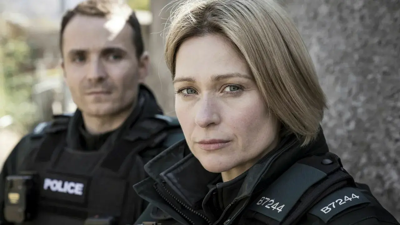 Två poliser i uniform, en kvinna i förgrunden med intensiv blick, bakgrunden svagt belyst av blåa ljus.