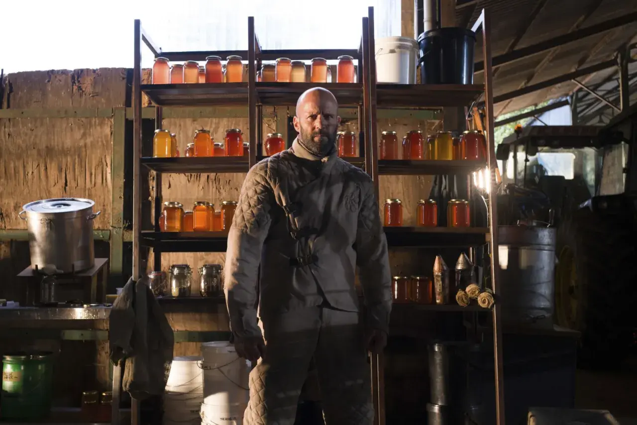 Jason Statham som rollistan i The Beekeeper, omgiven av burkar med honung och jordbruksutrustning.