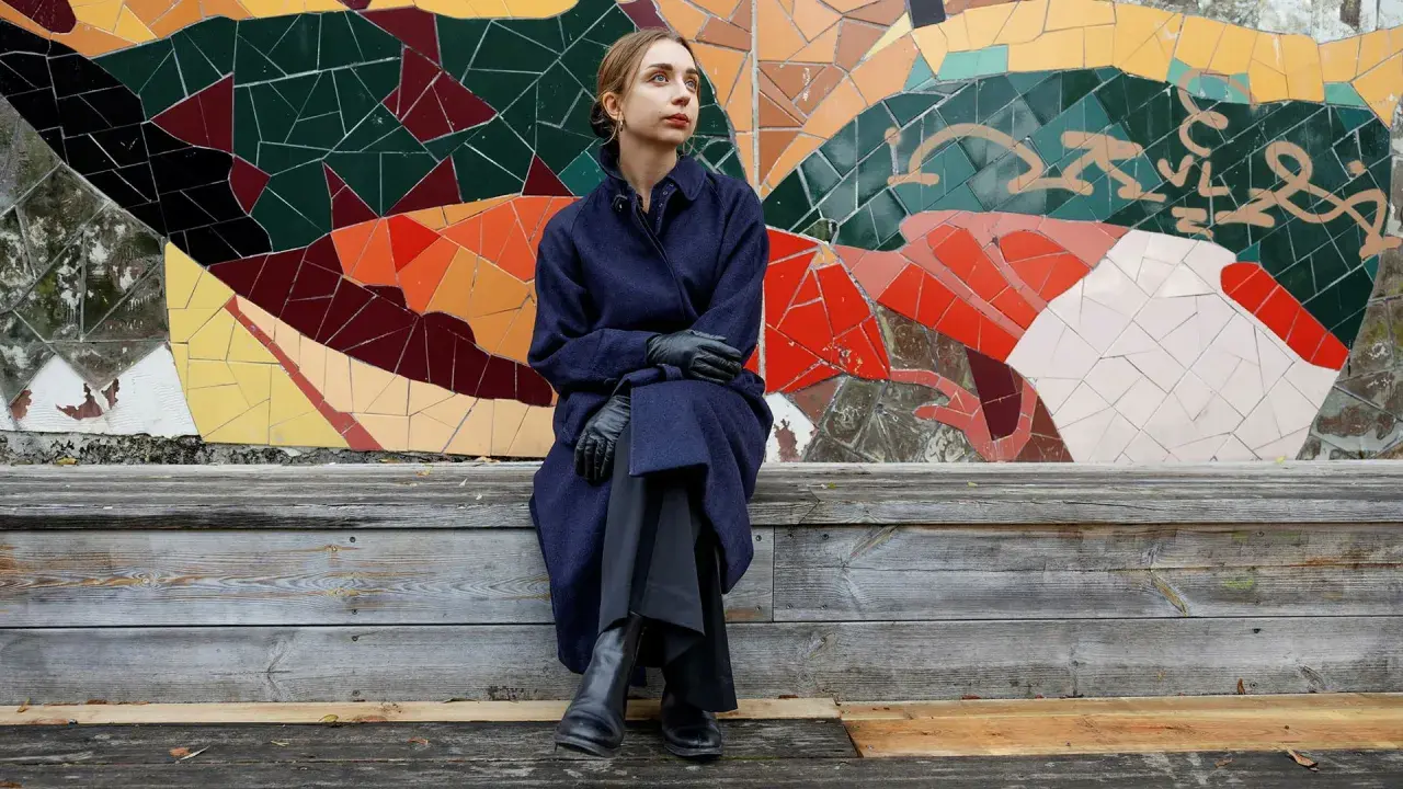 Alexandra Andersson sitter på en träbänk framför en färgglad mosaikvägg.