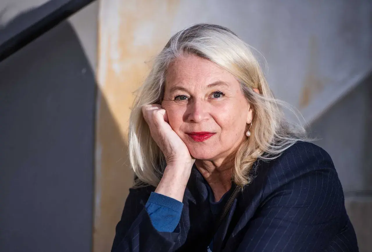 Helena von Zweigbergk, med sin partner vid sin sida, ler mot kameran. Hennes blonda hår ramar in ett ansikte med röda läppar och en pärlörhänge.